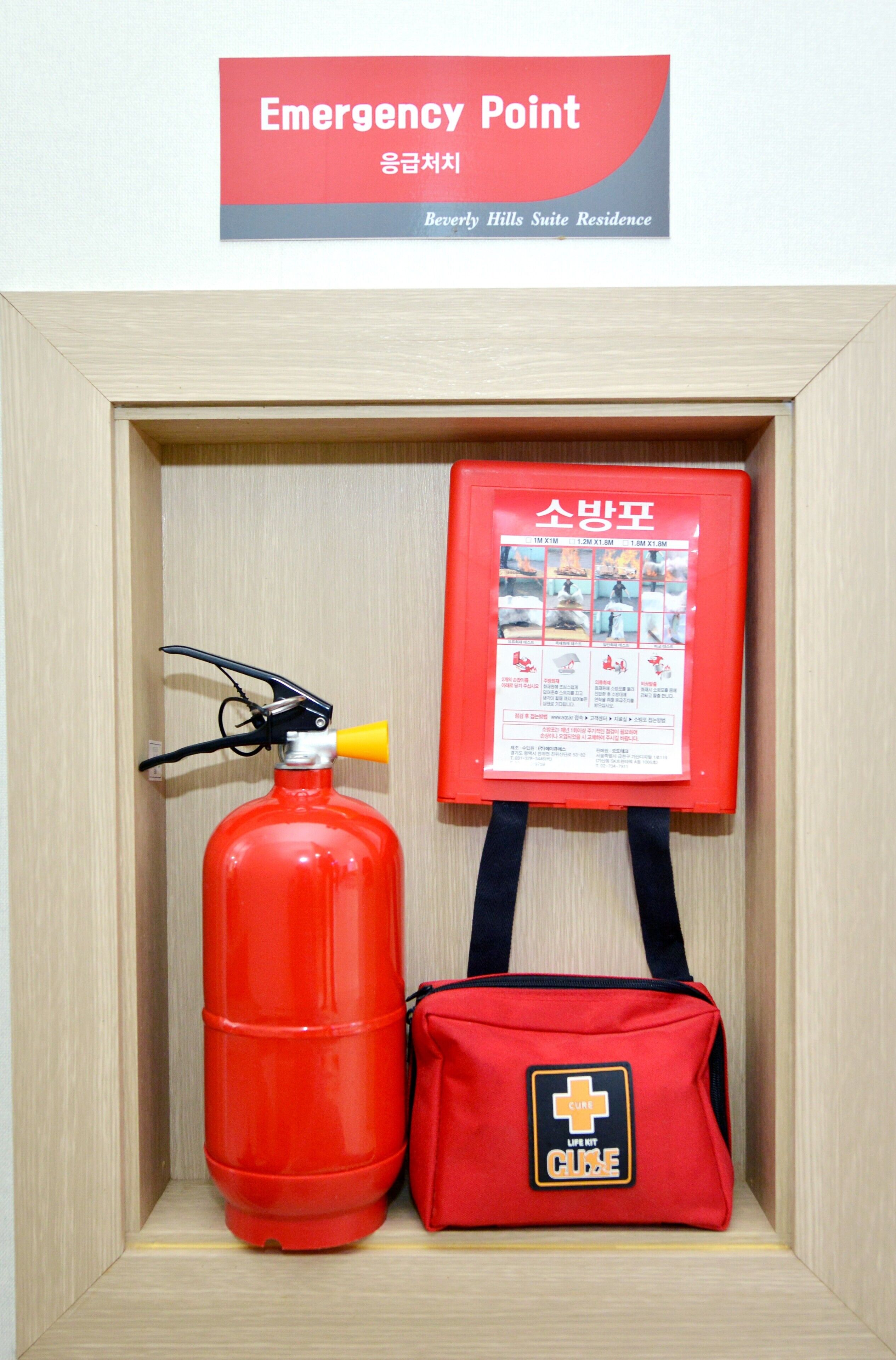Una señal de punto de emergencia enmarco, un extintor rojo y una bolsa roja de botiquín de primeros auxilios.