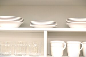 Una estantería con cuencos y tazas blancas apiladas.