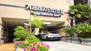 A hotel entrance with a sign in Korean and English, a white car parked in a covered parking area, and potted plants with pink flowers in front. - GeojeResidenceHotel (Geoje)