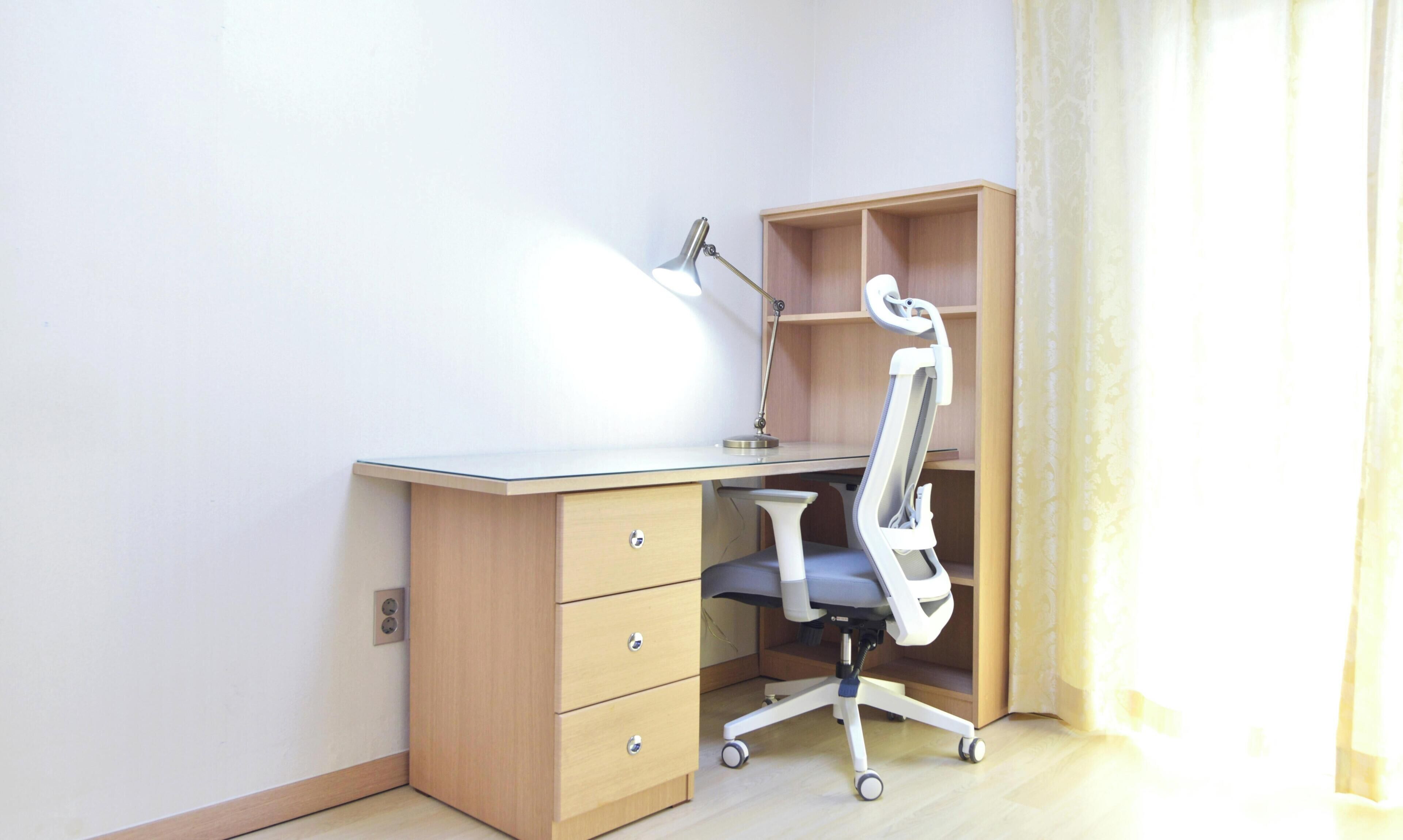 A corner office with a desk, chair, lamp, and shelving unit.