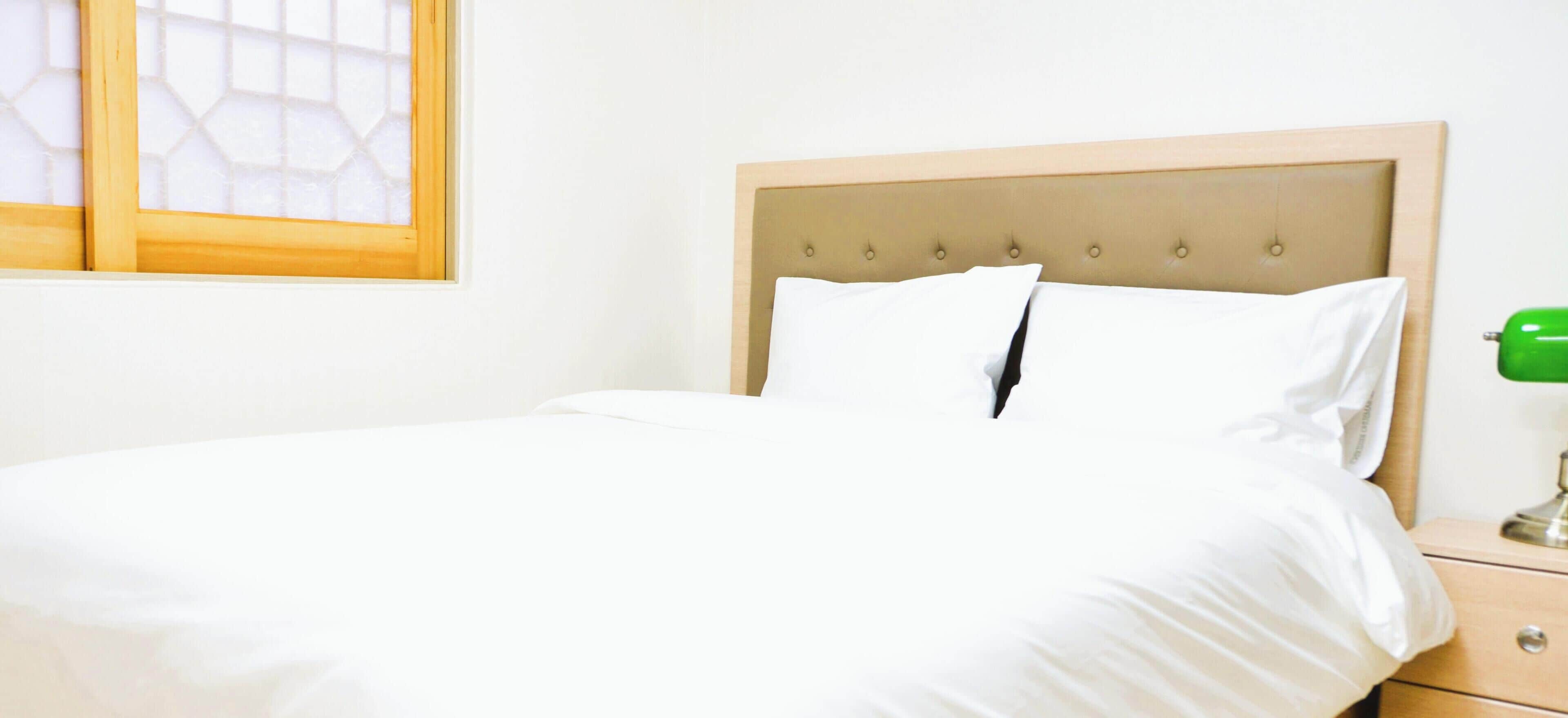 A neatly made bed with white linens, a wooden headboard, and a green lamp on a bedside table.