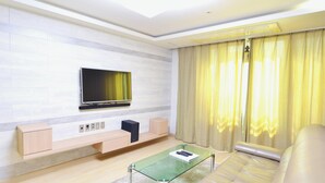 A modern living room with a flat-screen TV mounted on the wall, a glass coffee table, a sofa, and a light-colored floor. - GeojeResidenceHotel (Geoje)