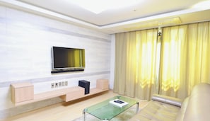 Una sala de estar moderna con un televisor de pantalla plana montado en la pared, una mesa de centro de vidrio, un sofá y un suelo de color claro.