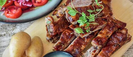 Une planche à découper en bois avec de la viande tranchée, des pommes de terre et un bol de sauce.
