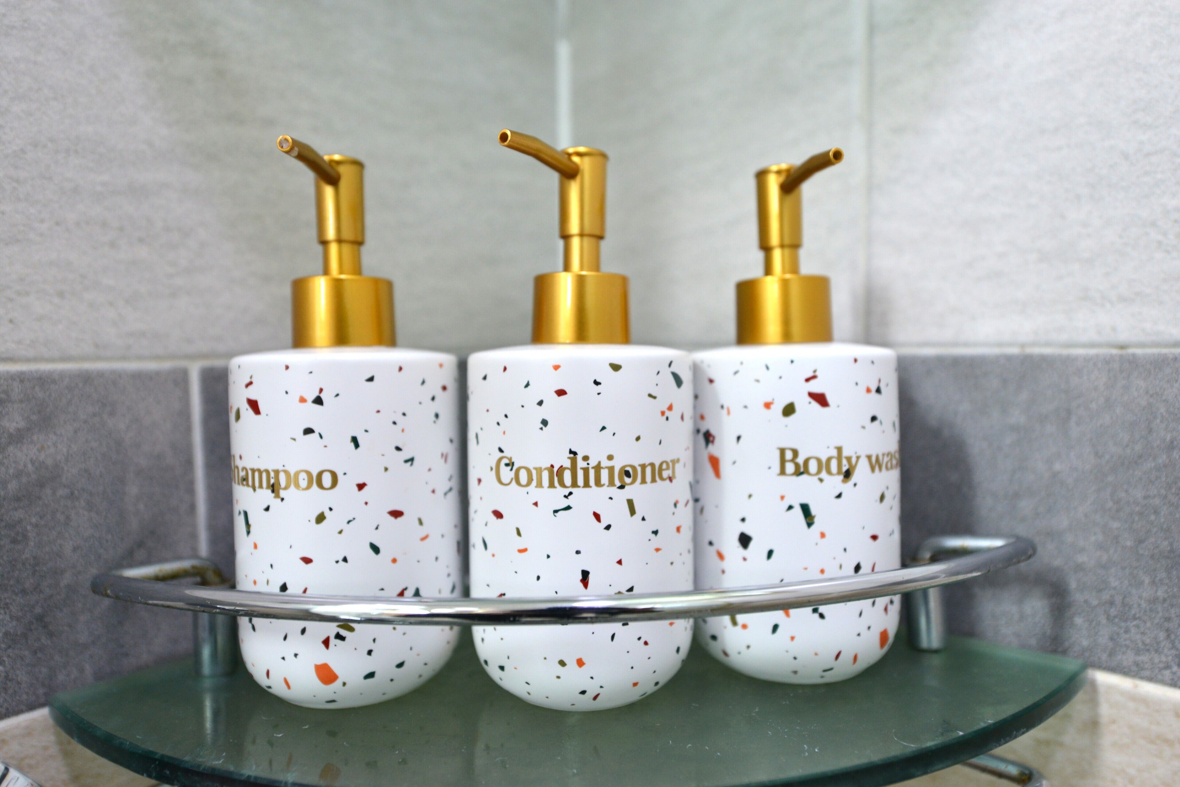 Three toiletry bottles with gold pumps on a glass shelf.