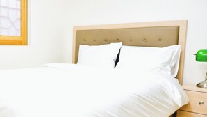 A neatly made bed with a wooden headboard, a bedside table with a green lamp, and a window with a geometric pattern. - GeojeResidenceHotel (Geoje)