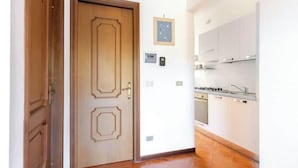 A hallway leading to a kitchen with white cabinets, a wooden door, and a framed picture on the wall. - Hostdomus - Olive Grove House (Laigueglia)
