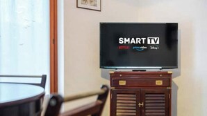A room with a television on a stand, a dining table, and chairs. - Hostdomus - Olive Grove House (Laigueglia)