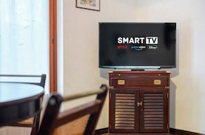 A room with a television on a stand, a dining table, and chairs. - Hostdomus - Olive Grove House (Laigueglia)