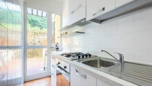 A modern kitchen with white cabinets, a gas stove, a sink, and a view through a glass door. - Hostdomus - Olive Grove House (Laigueglia)