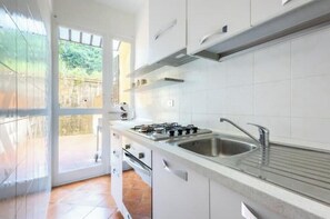 Una cucina moderna con mobili bianchi, un piano cottura a gas, un lavandino e vista attraverso una porta vetrata.