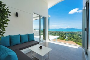 Ein modernes Wohnzimmer mit einer Couch, einem Couchtisch und einer großen Glastür, die auf einen Balkon mit Blick auf die Stadt führt.