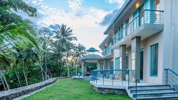 Um hotel moderno com área externa coberta, piscina e vegetação exuberante.