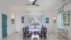 Un dormitorio con cama a dosel, dos sillones, una mesita con flores y un ventilador de techo.