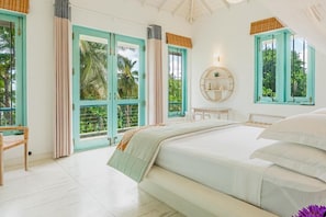 Un dormitorio con cama, una silla, un espejo redondo y vistas a zonas verdes por las ventanas.
