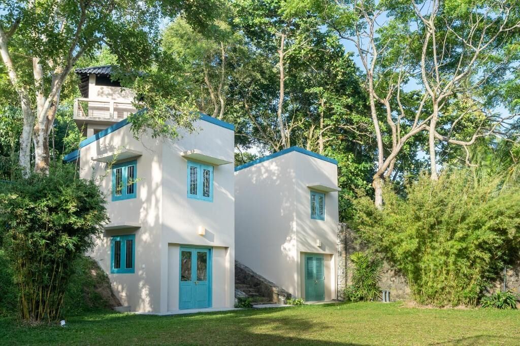 A two-story building with a white exterior and blue accents, surrounded by lush greenery.