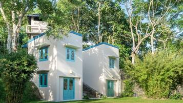 A two-story building with a white exterior and blue accents, surrounded by lush greenery.