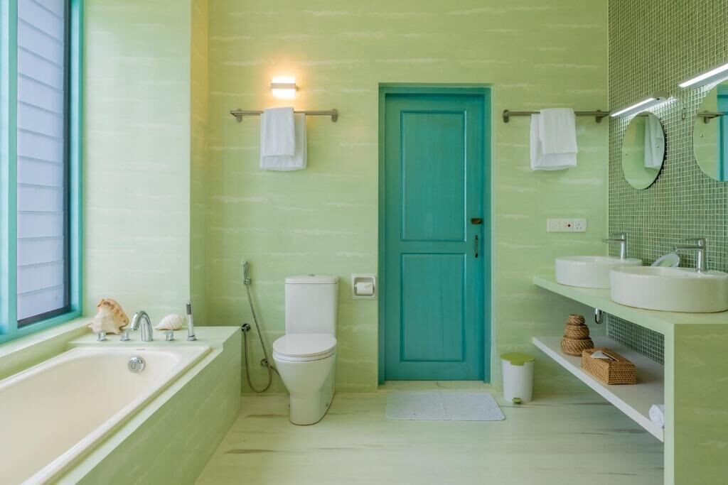 A bathroom with a bathtub, toilet, and sink, featuring a teal door and light green walls.