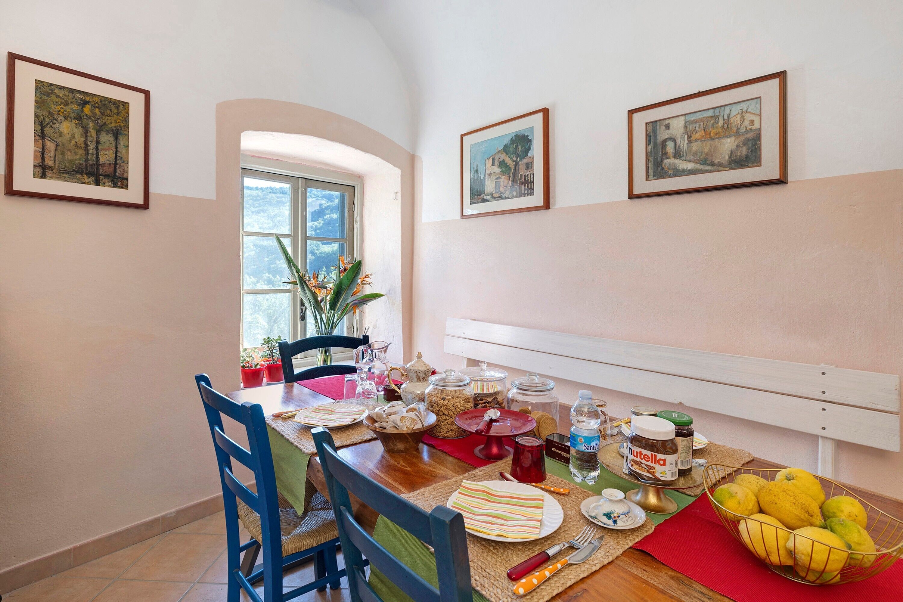 Un coin repas avec une table dressée pour quatre personnes, des chaises, une fenêtre et deux tableaux encadrés accrochés au mur.