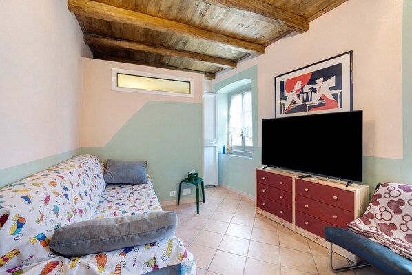 A room with a sofa, a television, a dresser, and a painting on the wall.