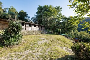 A rustic stone building with a sloped roof, surrounded by a grassy area and dense trees.