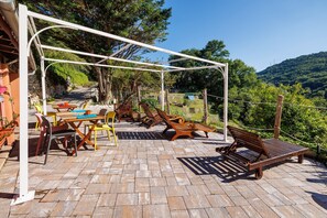 An outdoor patio with a pergola, seating, and a view of a hillside.