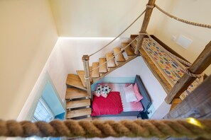 A wooden staircase leading to a bed with a red blanket and pillows.