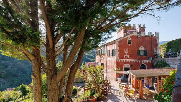 Un edificio rosso con un balcone, circondato da alberi e piante in vaso.