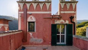 Un edificio rosso con una finestra e persiane verdi, una porta e un balcone con vista sulla campagna.