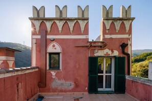Un edificio rosso con una finestra e persiane verdi, una porta e un balcone con vista sulla campagna.