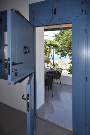 Een kamer met een blauwe deur die leidt naar een terras met uitzicht op zee.