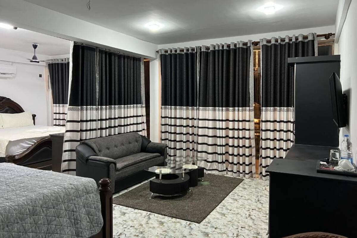 Una habitación de hotel con cama, sofá, televisión, escritorio y cortinas.