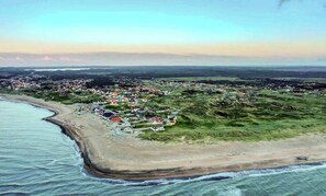 An aerial view of a coastal town with a beach, houses, and a hilly landscape. - In Cold Hawaii with beach in backyard (Thisted)
