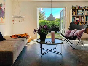 A living room with a sofa, a chair, a round table with a candle, a hanging light fixture, and a bookshelf. - In Cold Hawaii with beach in backyard (Thisted)