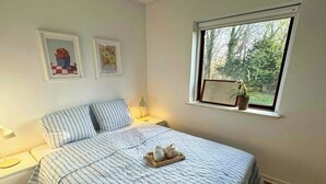 A bedroom with a bed, bedside tables, a window with a plant, and two framed pictures on the wall. - Summer house near bathing jetty at Fynshoved (Martofte)