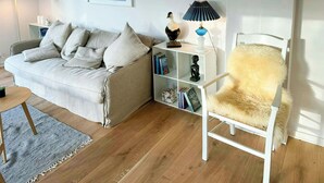 A living room with a sofa, a white armchair, a bookshelf, and a lamp. - Summer house near bathing jetty at Fynshoved (Martofte)