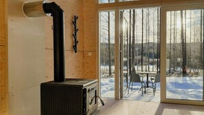 A wooden interior with a wood-burning stove, a glass door leading outside, and a view of a snowy landscape. - Minimalist cabin with forest views in Arvika (Arvika)