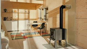 A modern kitchen with wooden walls, a dining area with chairs, a stove, and a window. - Minimalist cabin with forest views in Arvika (Arvika)