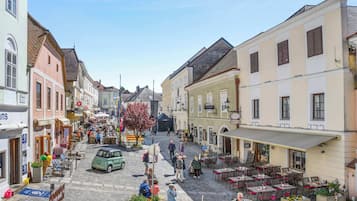 A cobblestone street with outdoor seating, buildings with signage, and a vintage car.