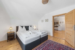 Une chambre avec un lit, des tables de chevet, un tapis et une vue sur la cuisine.