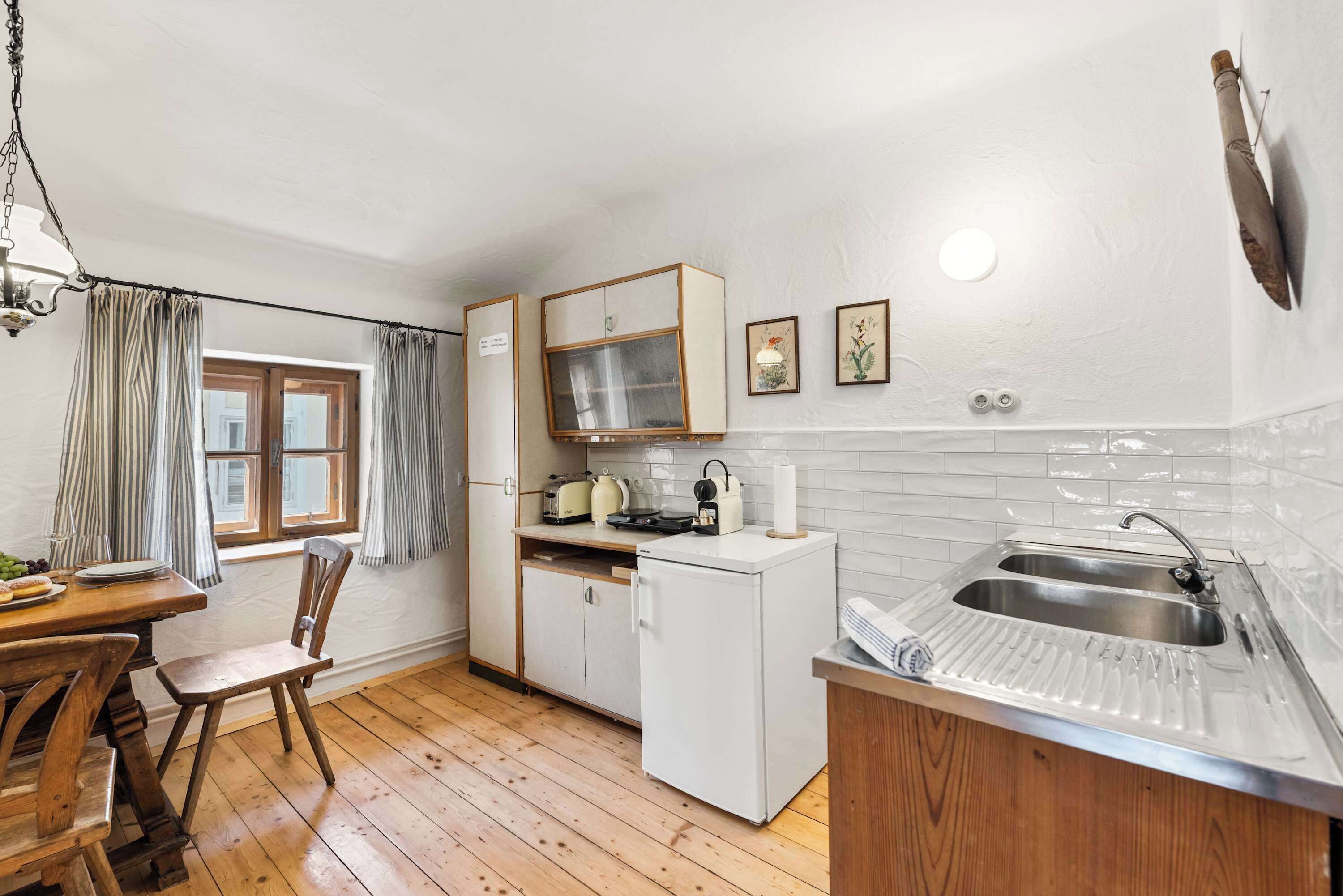 Una cocina compacta con piso de madera, un refrigerador blanco, un lavamanos y un comedor con mesa y sillas.