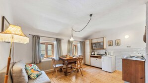 A cozy kitchen with wooden flooring, a dining table with chairs, a sofa with a patterned cushion, and a hanging lamp.