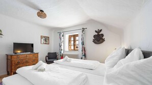 A bedroom with two beds, a dresser, a chair, a television, a window with curtains, and a coat rack.