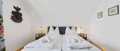 A room with two beds, white bedding, a coat of arms on the wall, and two bedside lamps.