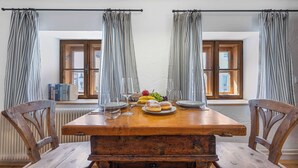 A dining table with chairs, a fruit plate, and a window with curtains.