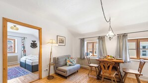 A room with a sofa, a dining table with chairs, a hanging light fixture, and a window with curtains.