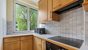A kitchen with wooden cabinets, a black stove, and a window with a view of trees.