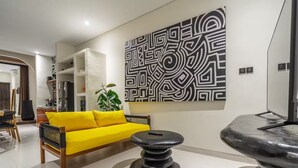 A living room with a yellow sofa, a black coffee table, and a large abstract wall art piece. - Alisa 4 Villa (Kerobokan)