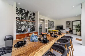 Zona de menjador moderna amb una taula de fusta llarga, cadires negres i un disseny geomètric a la paret en blanc i negre.