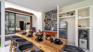 A modern kitchen with a dining table set for four, a refrigerator, and a decorative wall. - Alisa 4 Villa (Kerobokan)